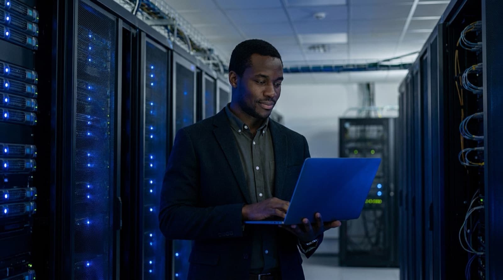 A Black African IT professional checking systems on a laptop in a server room